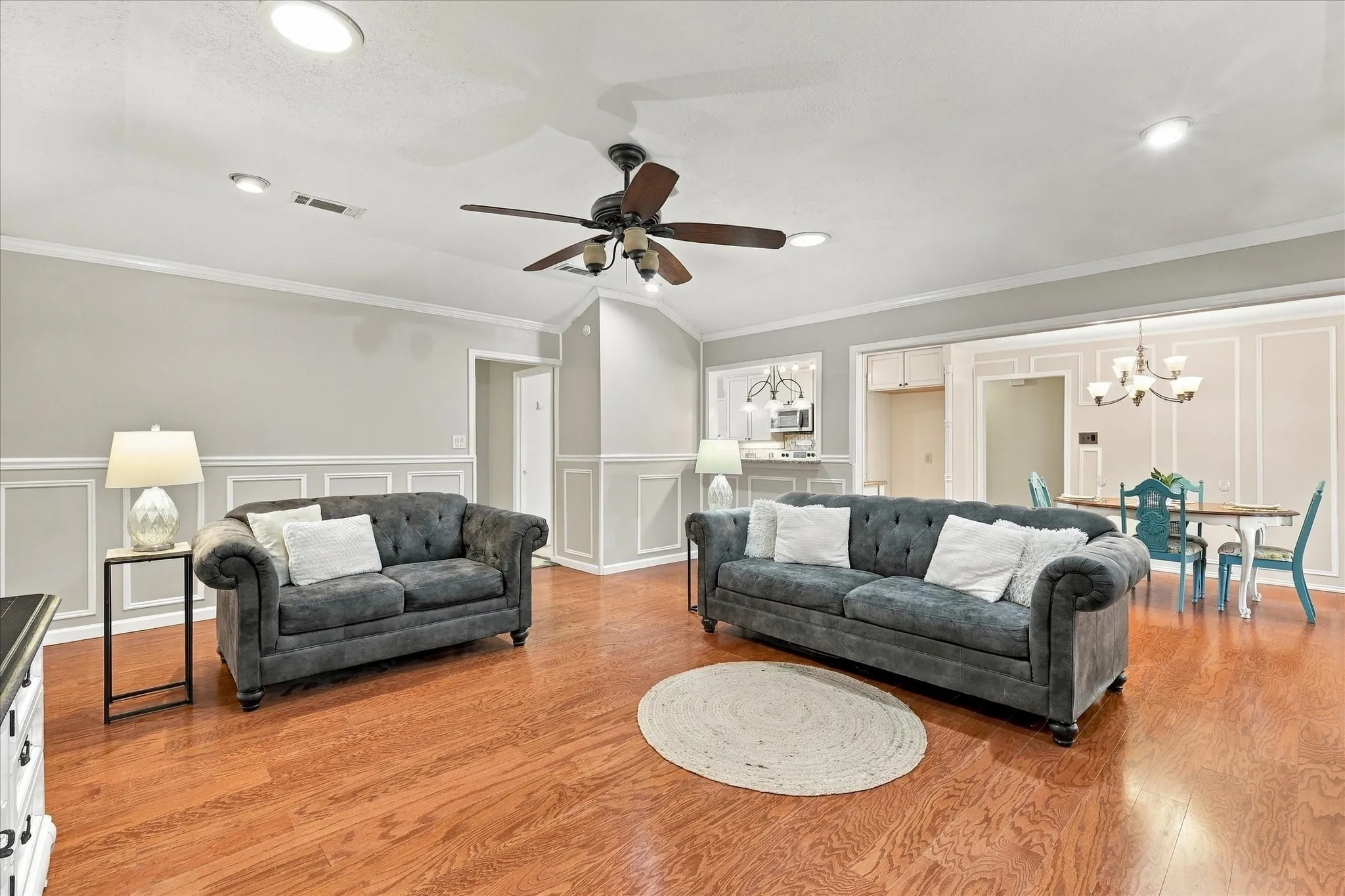 Spacious living area featuring wood-finish flooring, wainscoting, crown molding, a ceiling fan, and recessed lighting
