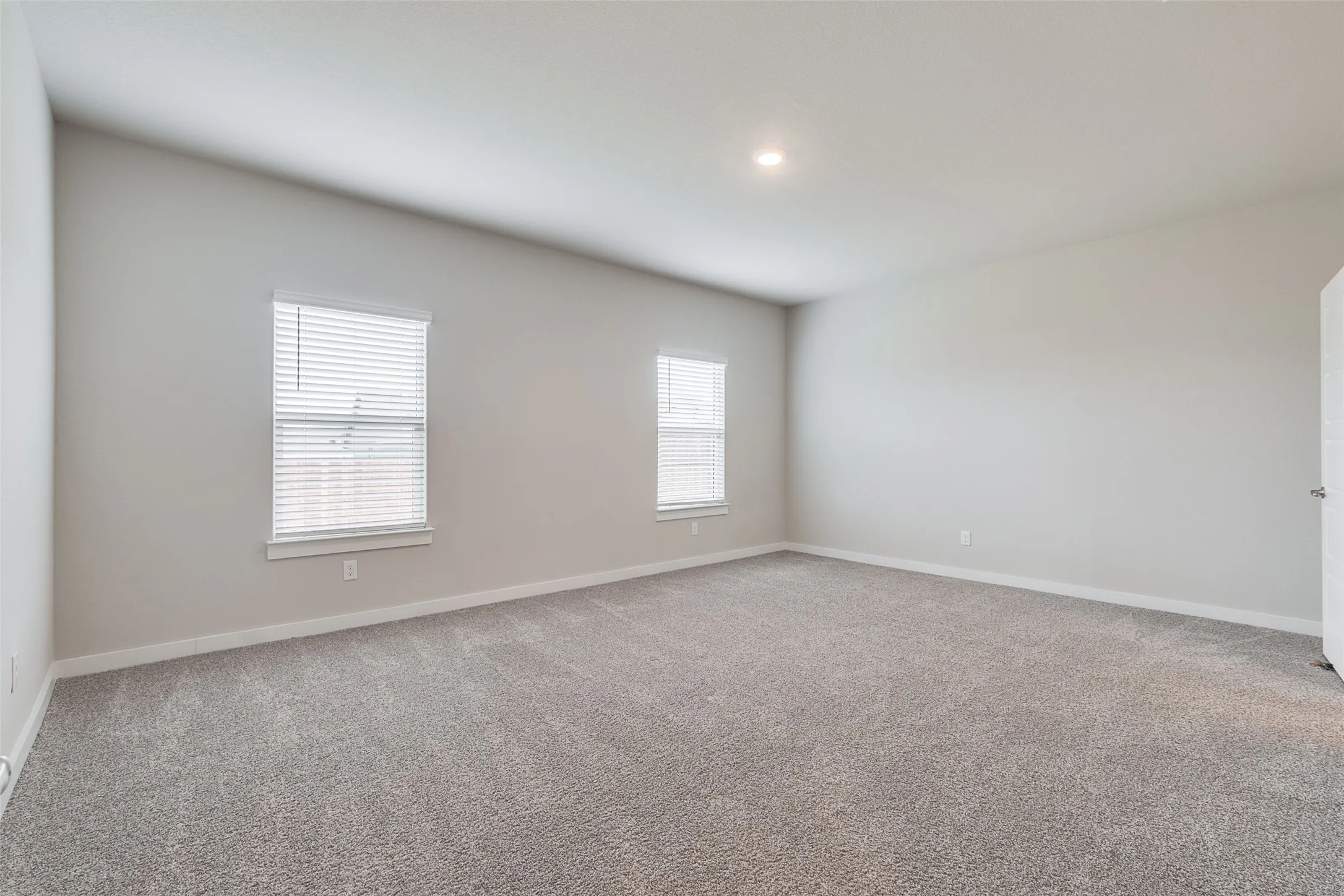 Spacious room featuring neutral carpeting, light-colored walls, two windows with blinds, and recessed lighting