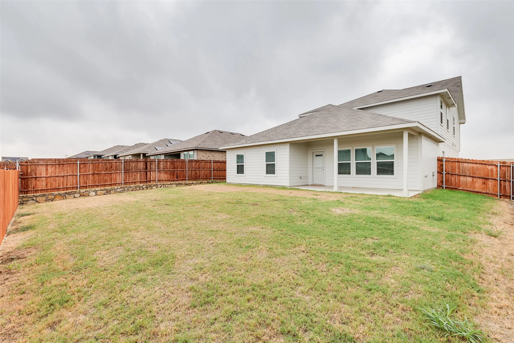 Expansive backyard with a wood privacy fence, concrete patio, and a covered porch