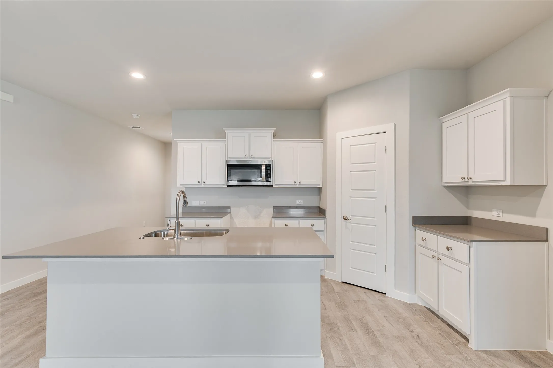 Kitchen featuring a large island with an undermount sink, white cabinetry, dark countertops, built-in microwave, and wood-finish flooring