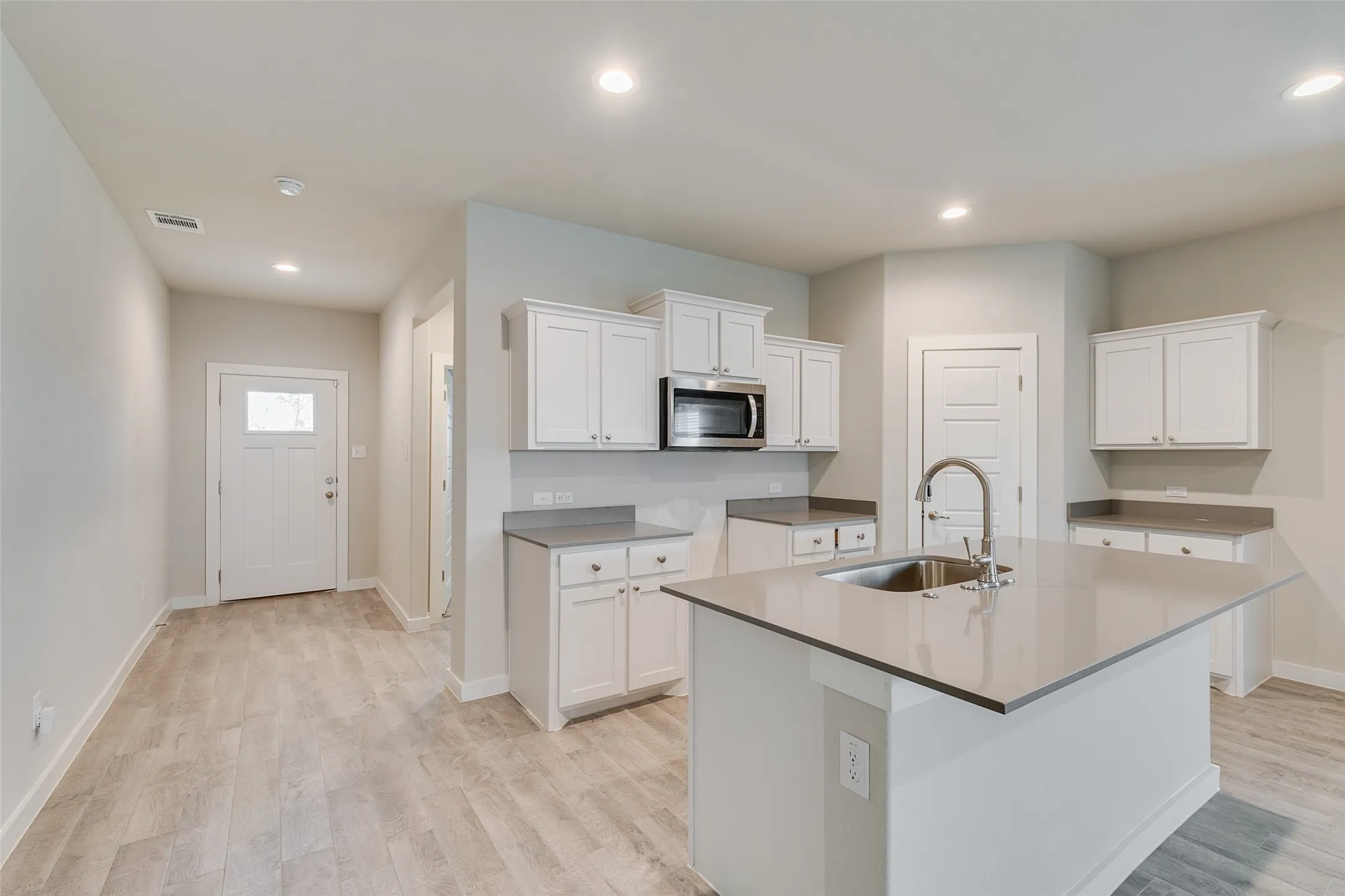Kitchen featuring a center island with an undermount sink, gooseneck faucet, white shaker cabinetry, and stainless steel microwave