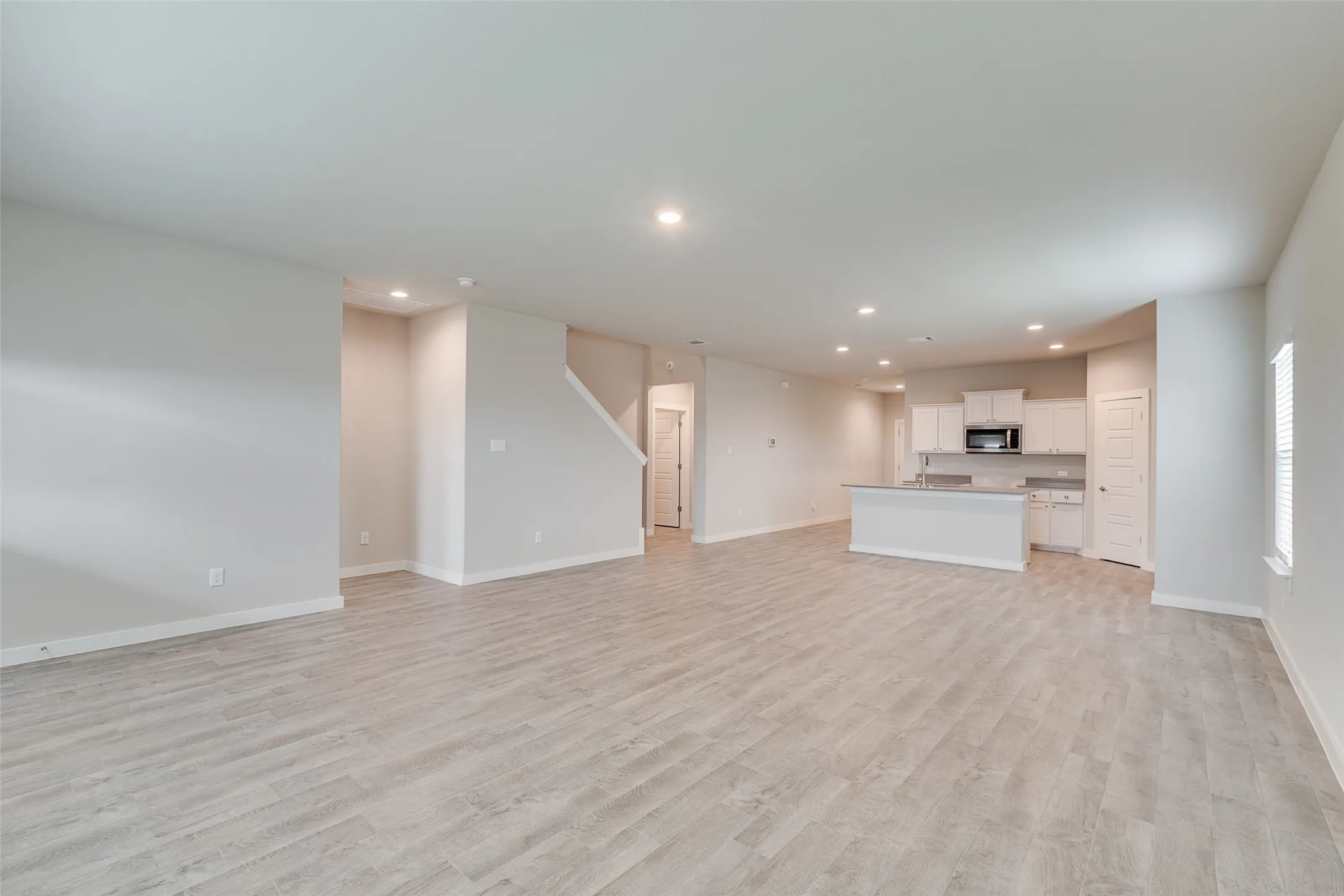 Open-concept living space featuring wood-finish flooring, recessed lighting, a kitchen island, and white cabinetry