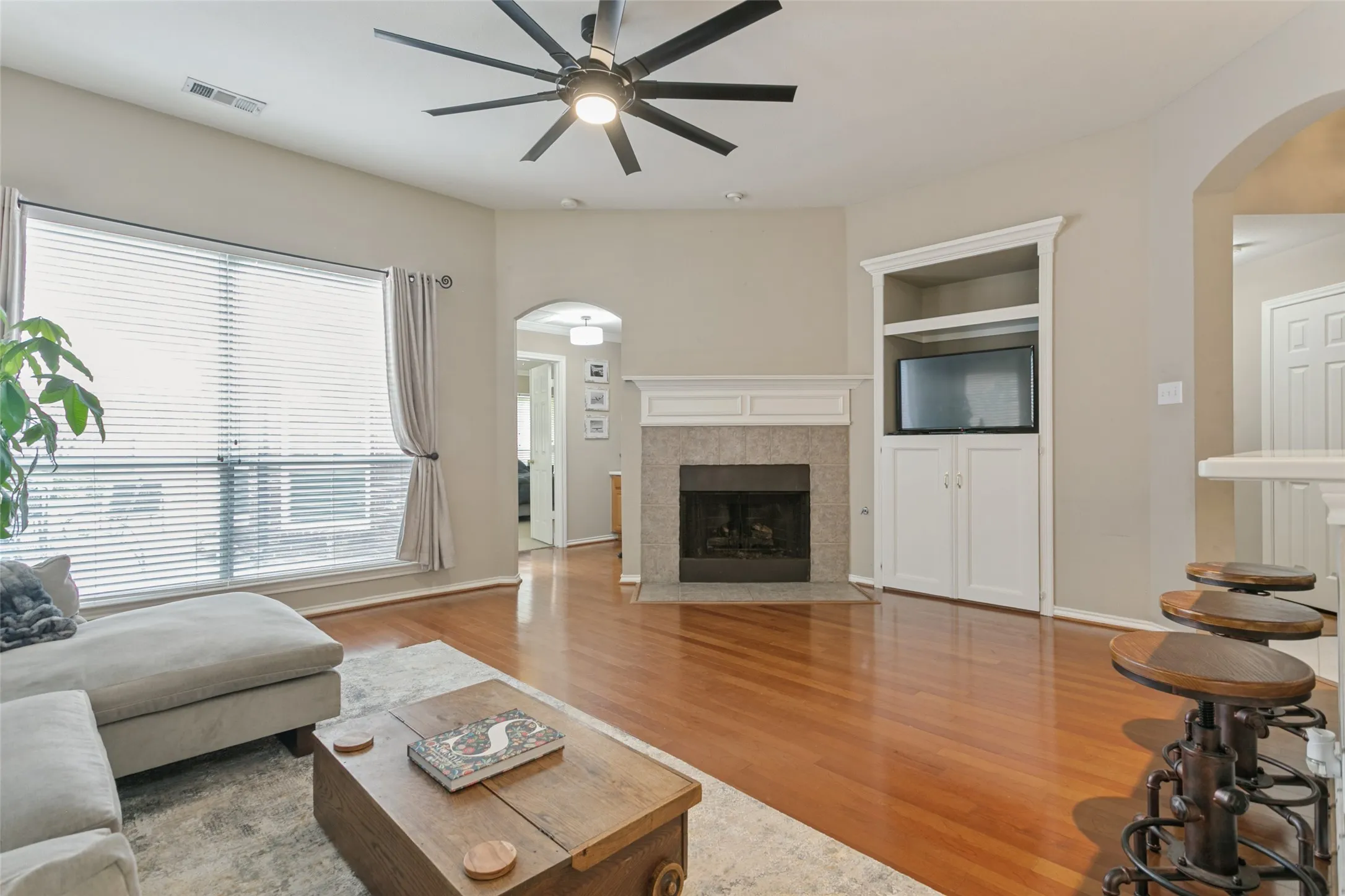 Hardwood flooring, ceiling fan, fireplace with mantel, built-in cabinetry, and window with blinds