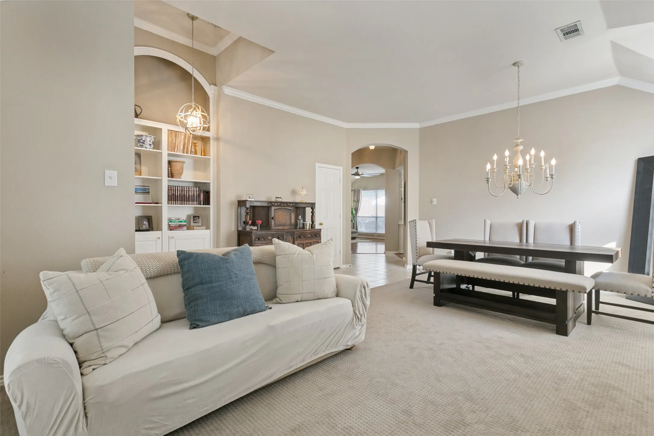 Built-in shelving with integrated lighting, vaulted ceiling, crown molding, arched entryways, and carpeted flooring