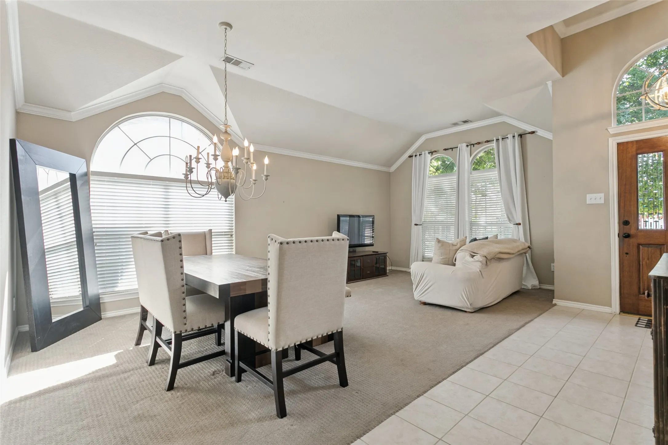 Vaulted ceilings, crown molding, arched windows, chandelier lighting, and a wood entry door