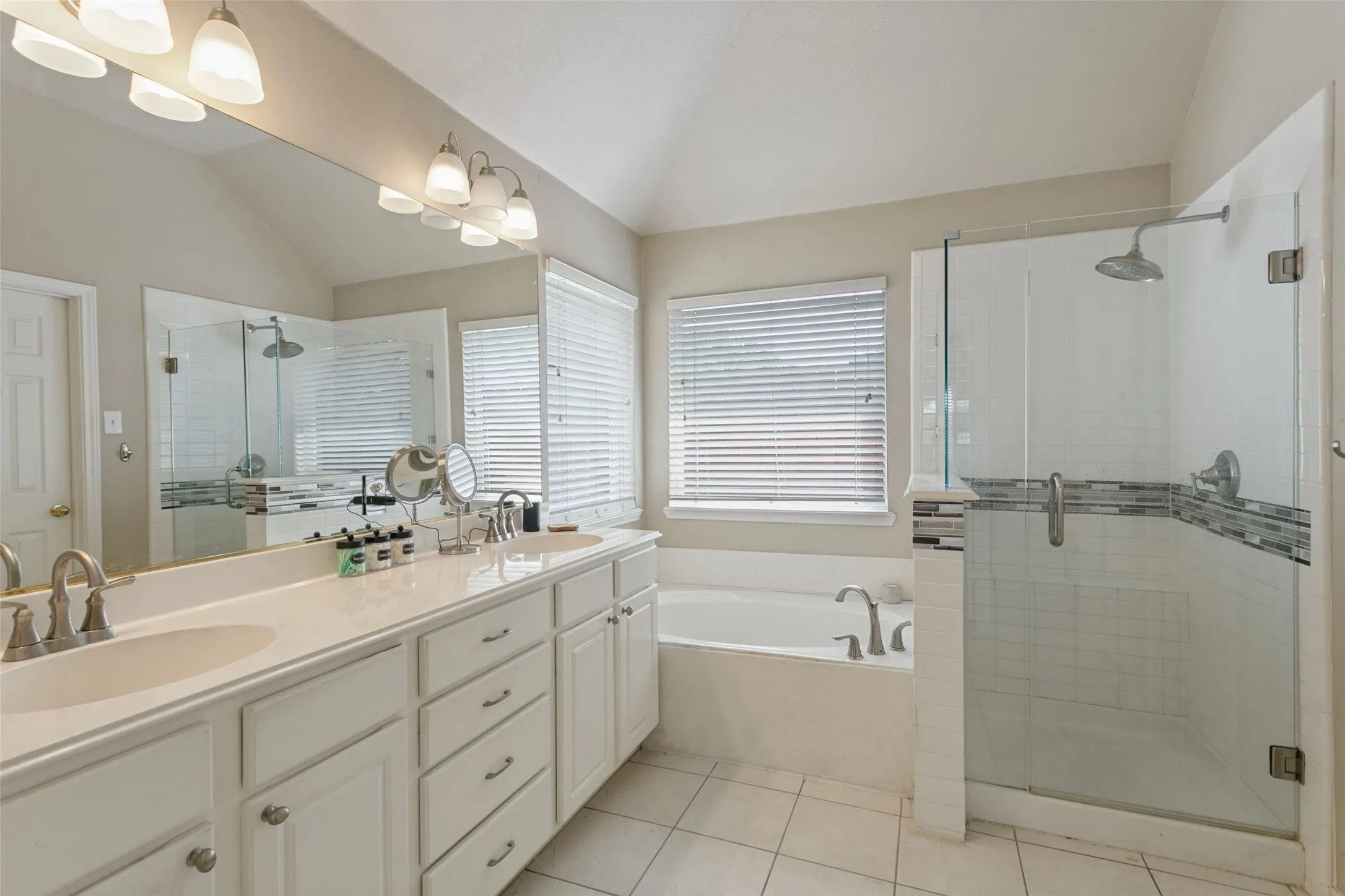 Dual vanity with undermount sinks, a built-in soaking tub, a separate glass-enclosed shower, and a vaulted ceiling