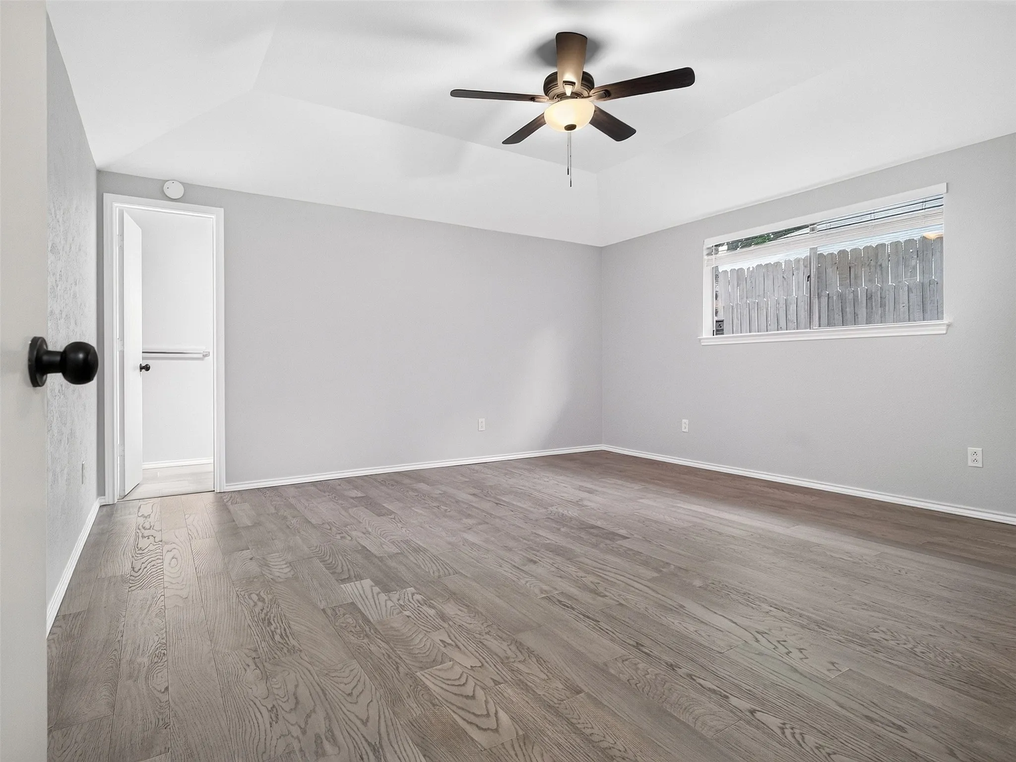 Tray ceiling, ceiling fan with integrated lighting, wood-finish flooring, single window, and neutral wall tones
