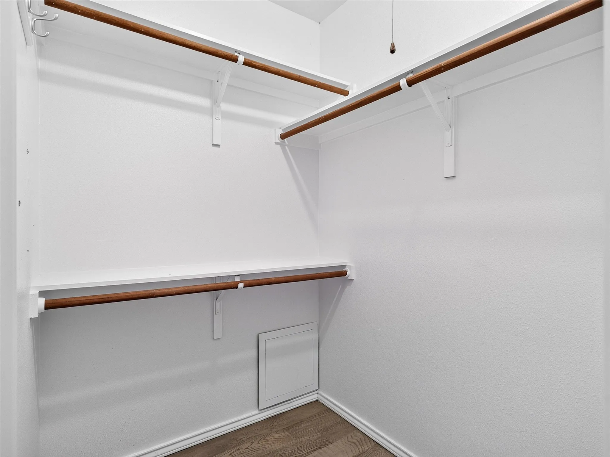 Built-in shelving and hanging rods in a white-painted closet with wood-finish flooring