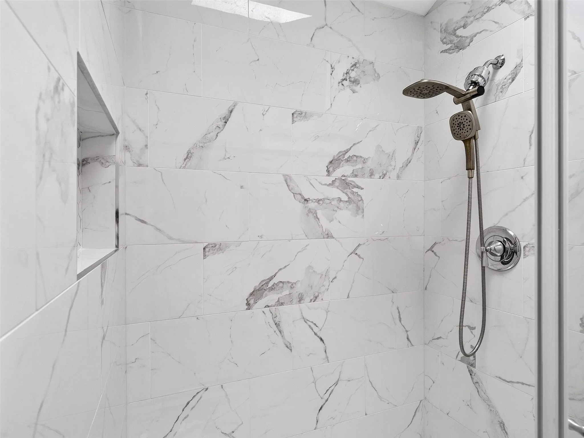 Tiled shower enclosure featuring a built-in niche, dual shower heads, and chrome fixtures