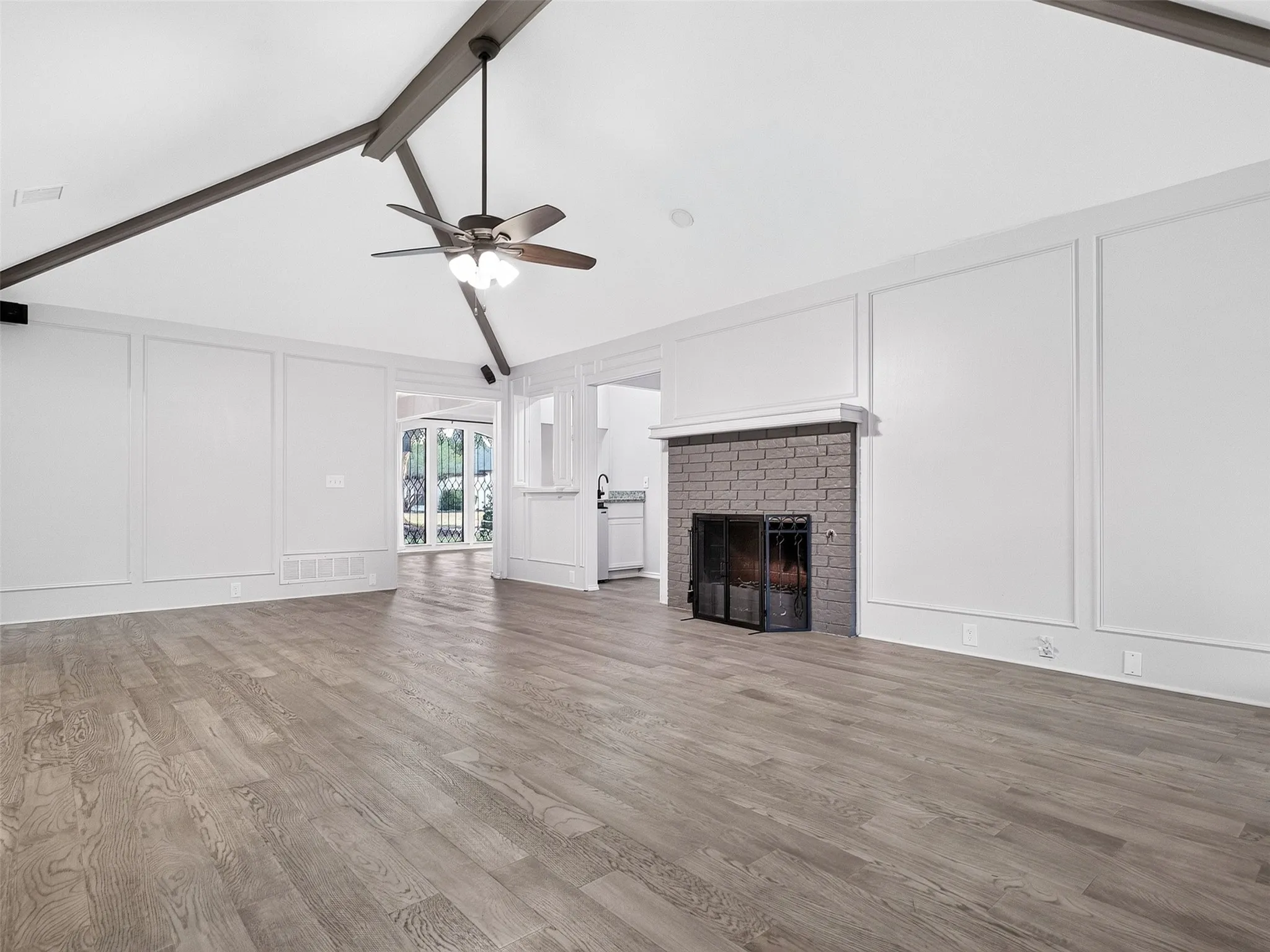 Vaulted ceiling with exposed beams, wood-finish flooring, brick fireplace with a metal screen, and decorative wall molding