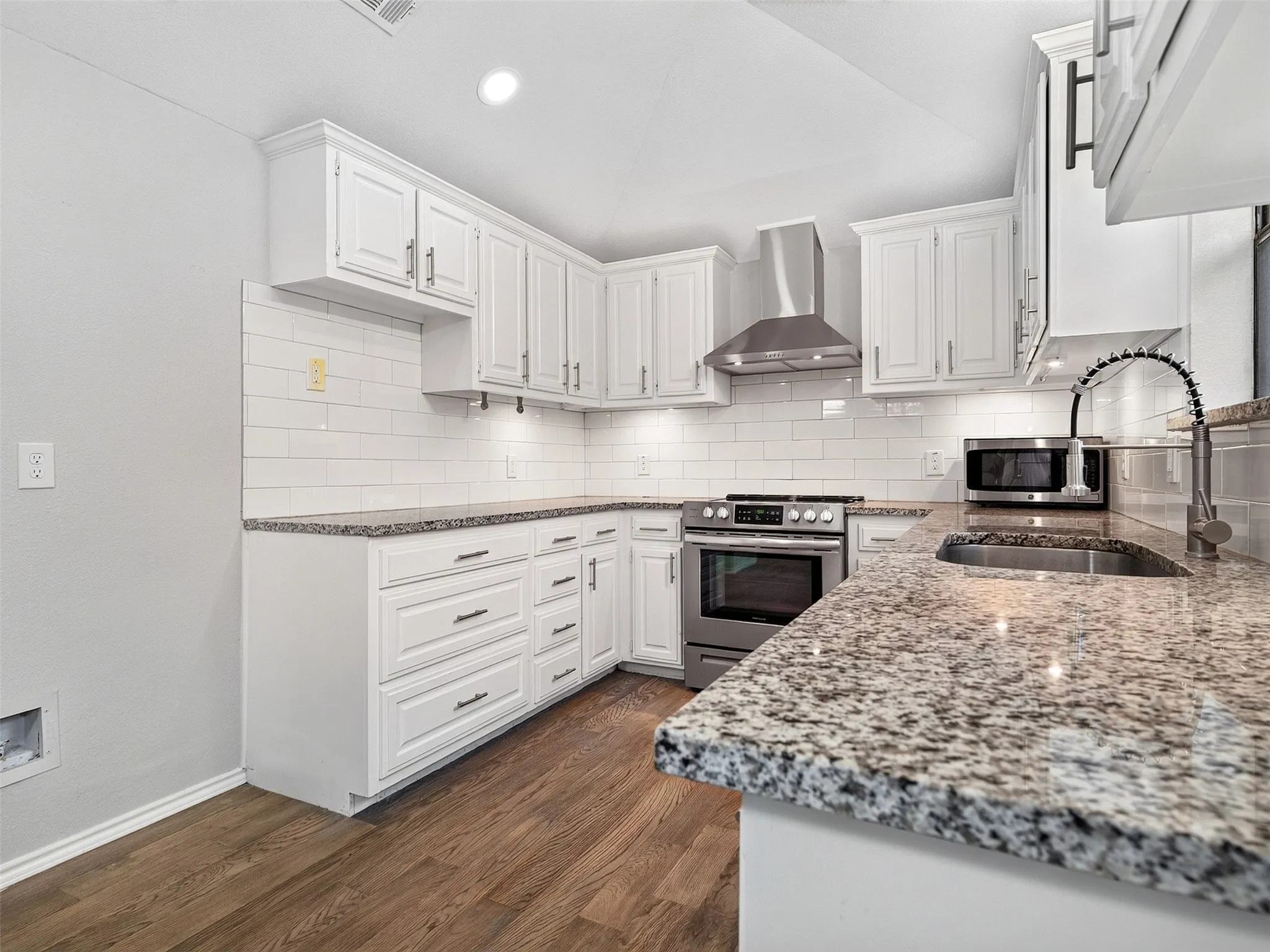 Kitchen featuring granite countertops, white cabinetry, stainless steel appliances, a subway tile backsplash, and wood-finish flooring