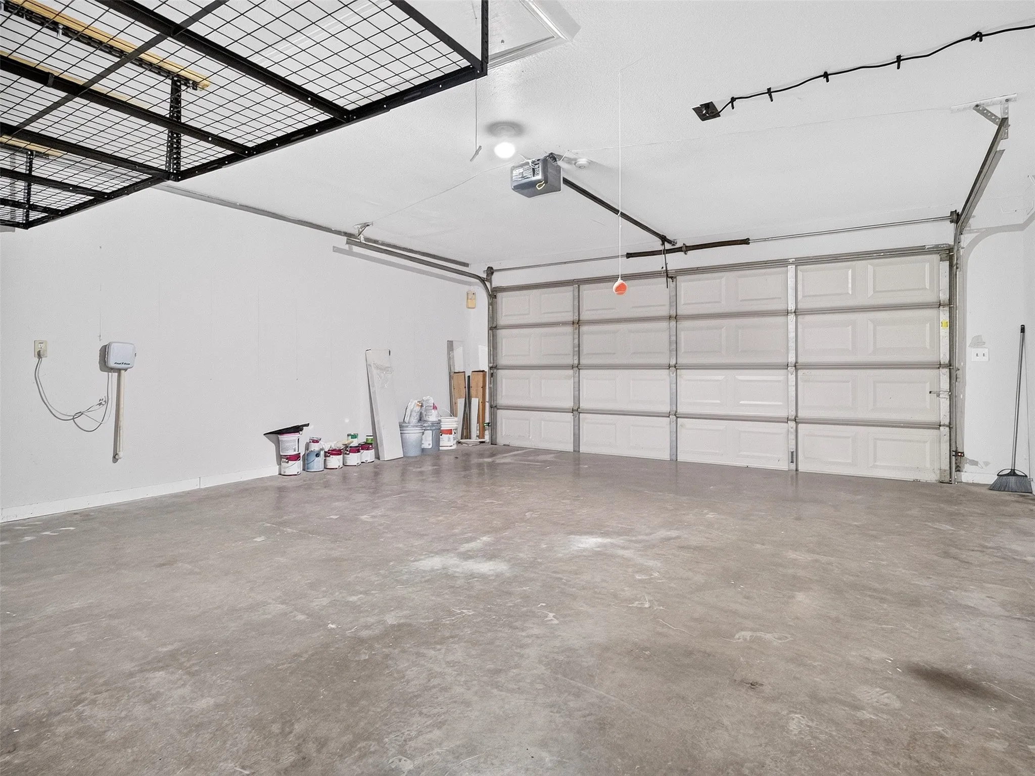 Concrete flooring and white walls in a spacious garage with an overhead garage door and ceiling-mounted storage racks