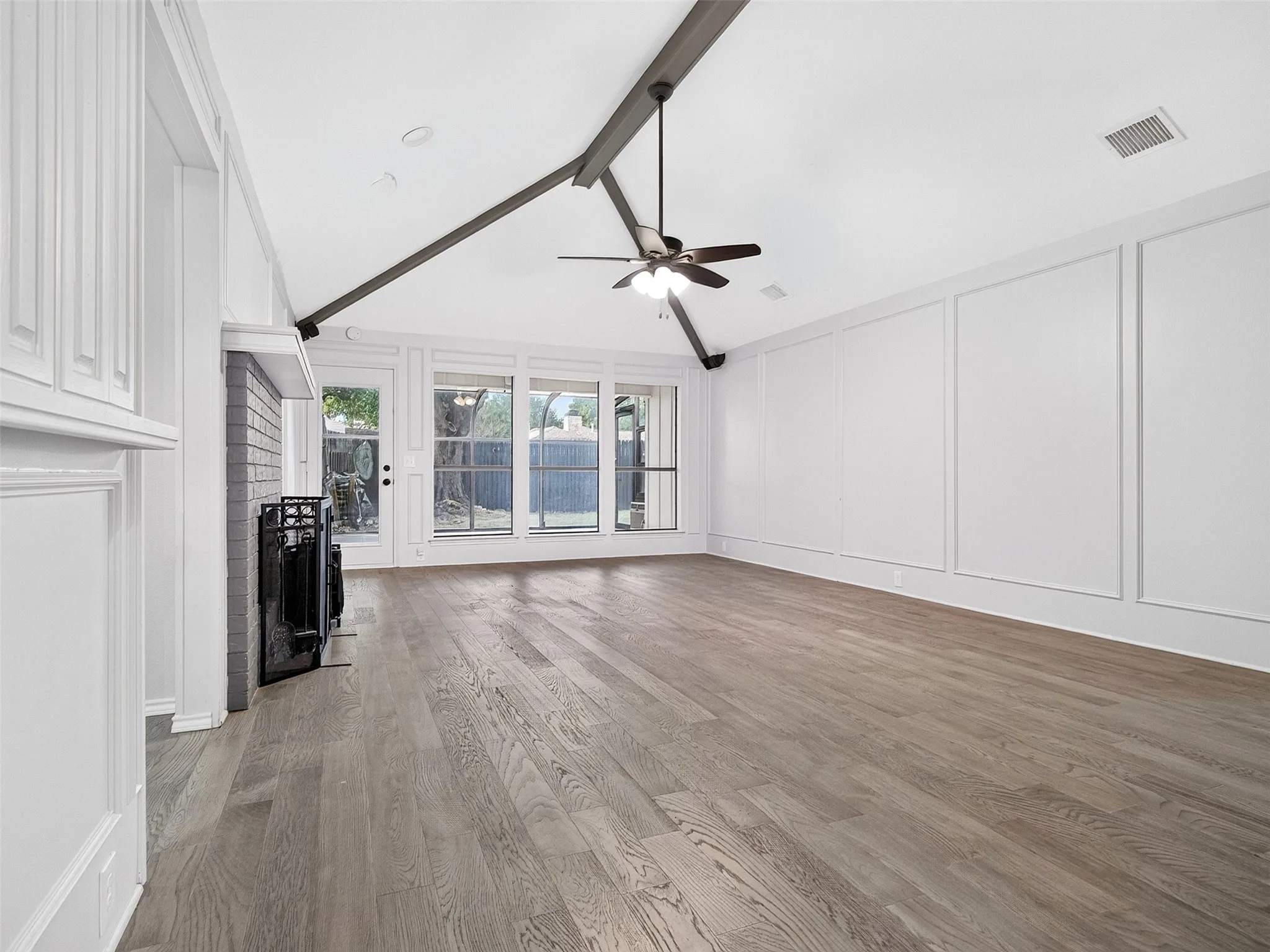 Vaulted ceiling with exposed beam, wood-finish flooring, fireplace with brick surround, built-in cabinetry, and large windows