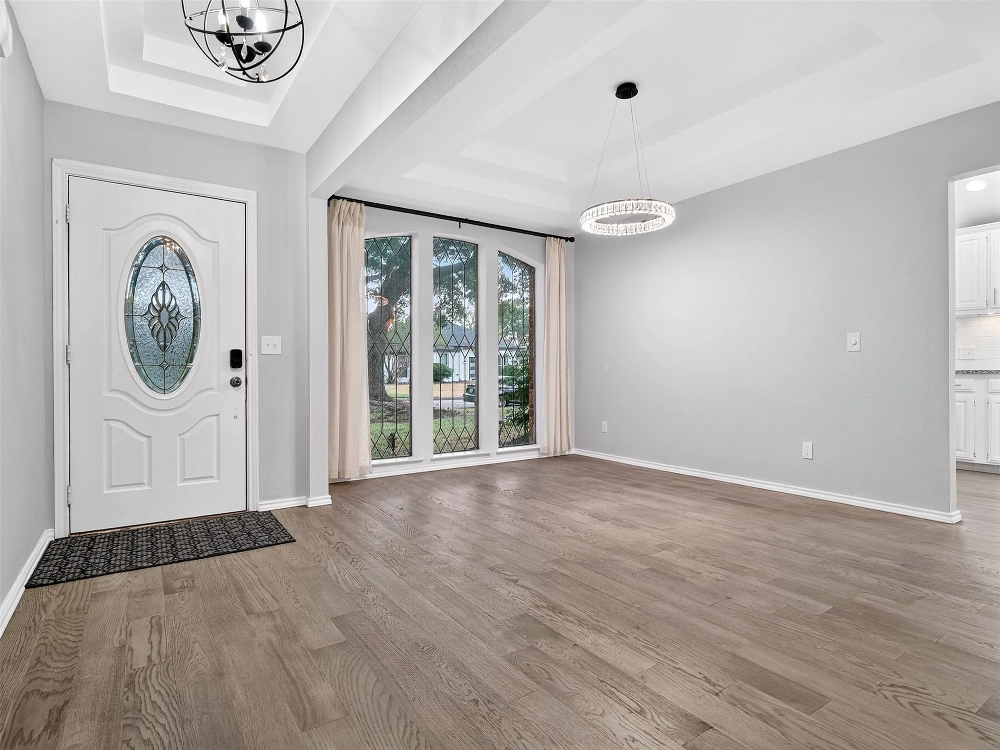 Light wood-finish flooring with a white entry door featuring decorative glass