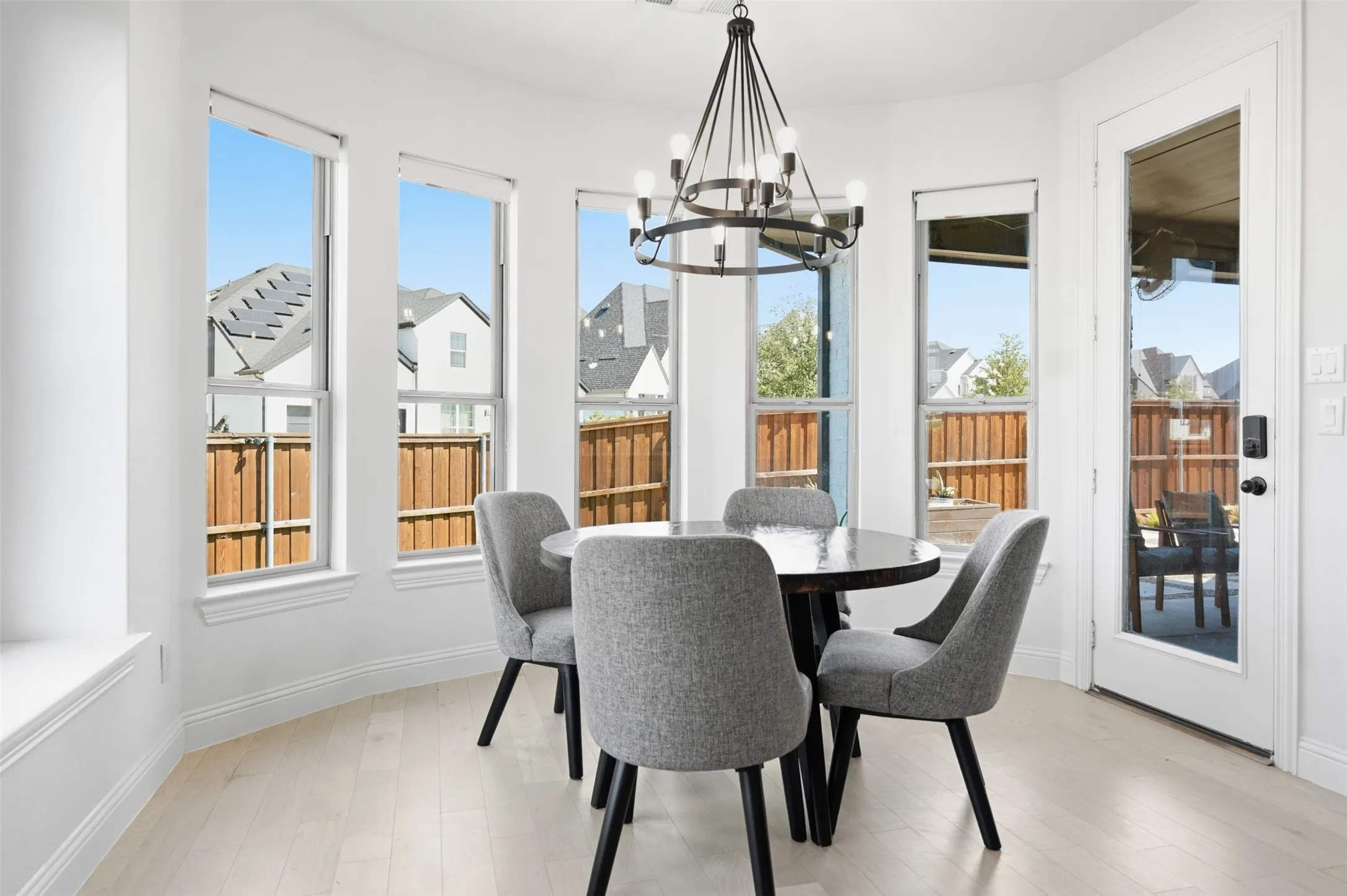 Bay window wall with light wood-finish flooring, a contemporary chandelier, and a glass-paneled door
