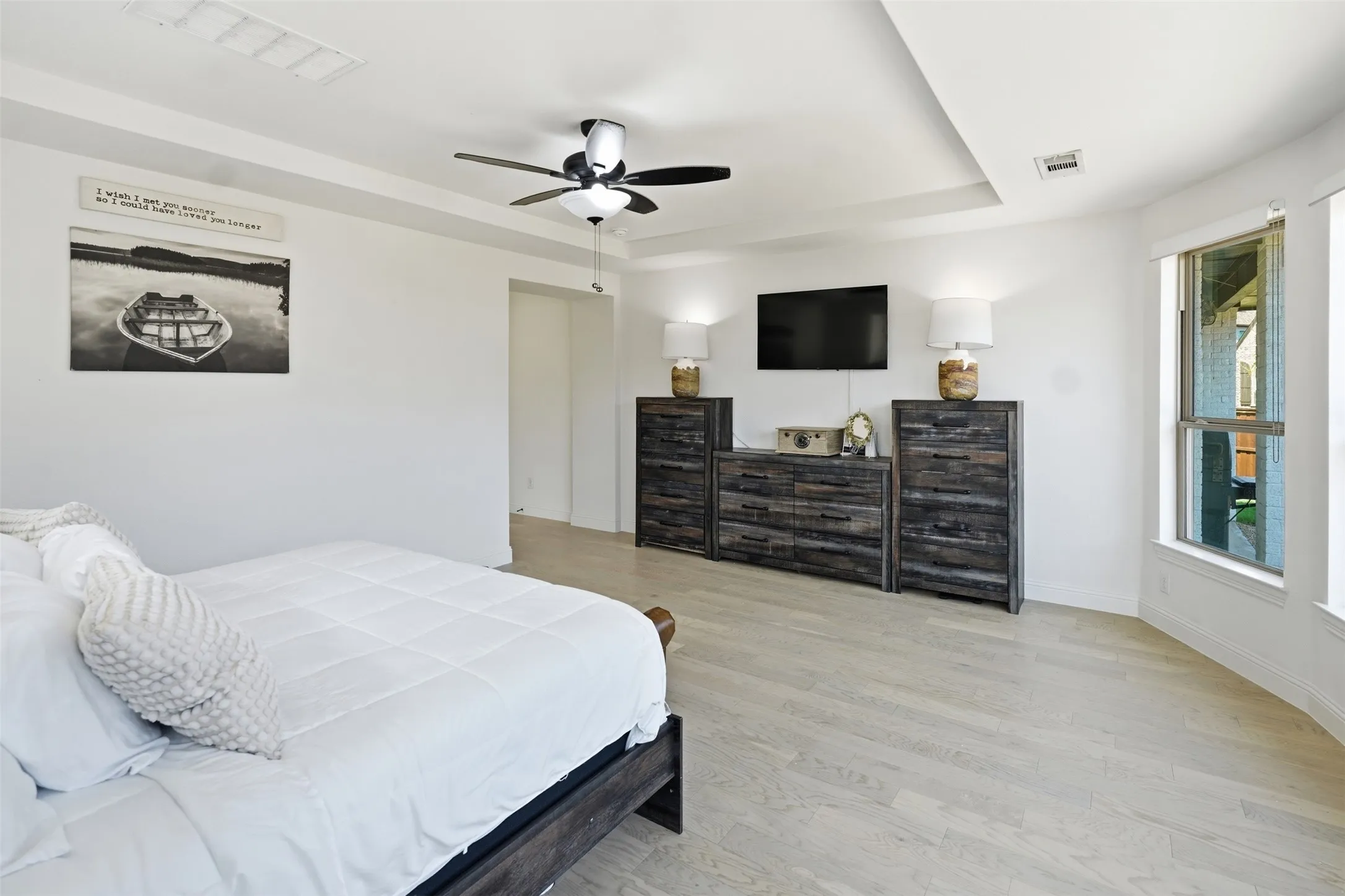 Tray ceiling with a ceiling fan, wood-finish flooring, and bay windows