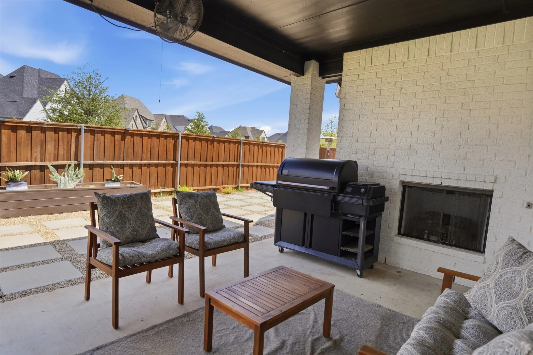 Covered outdoor living area featuring a built-in fireplace with a glass enclosure, white brick wall, and concrete patio