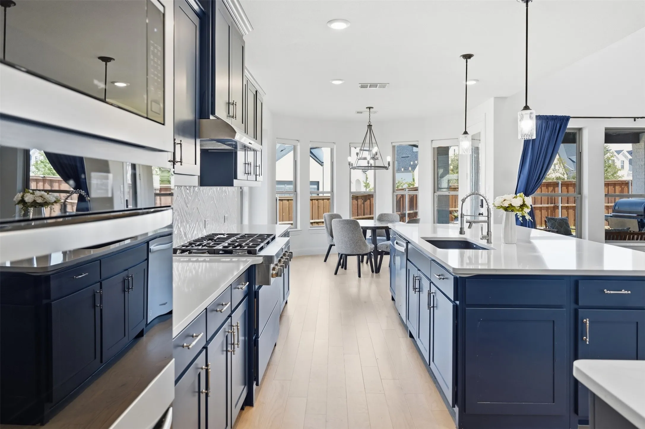 Open concept kitchen featuring dark blue cabinetry, light wood-finish flooring, white countertops, stainless steel appliances, and suspended pendant lighting