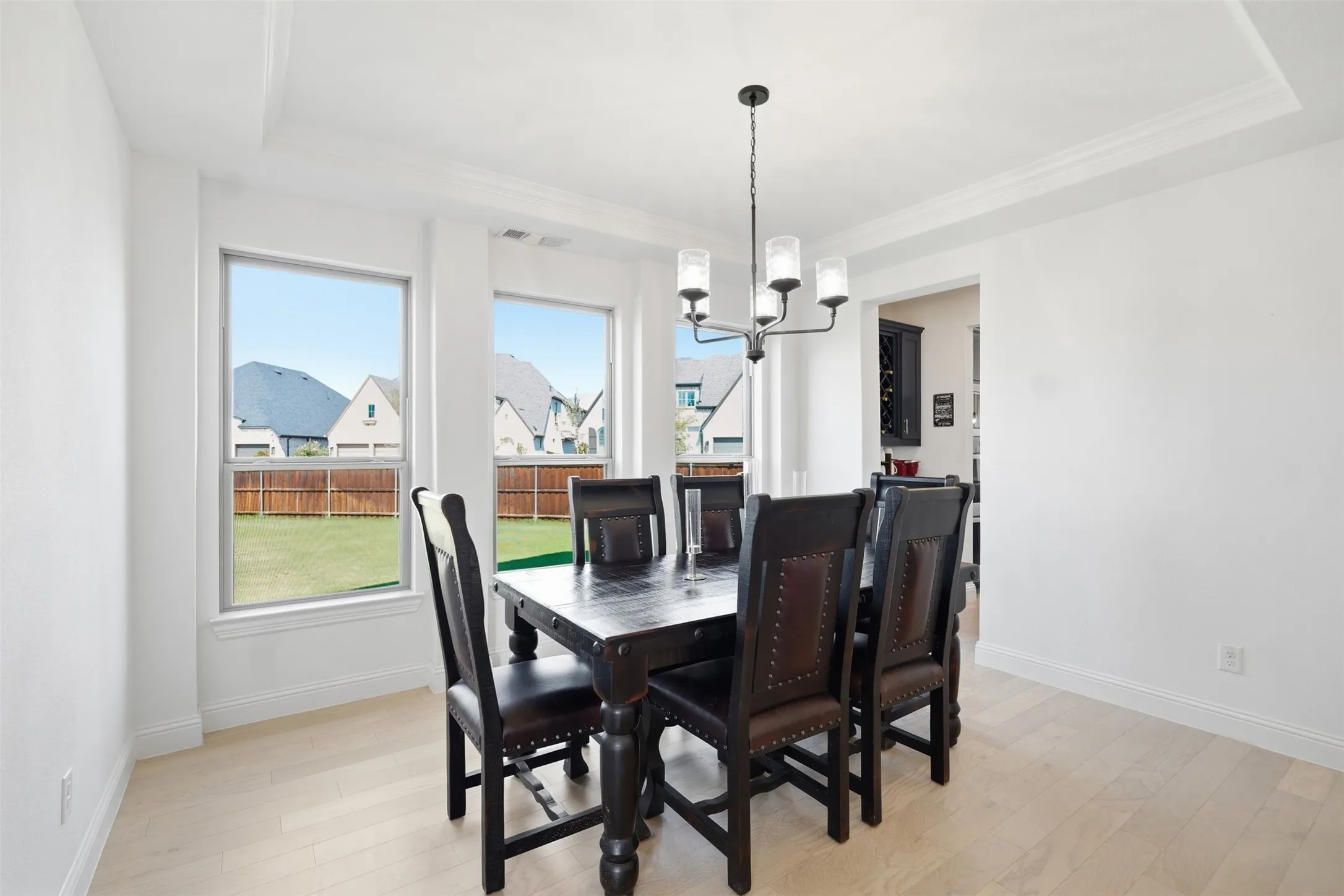 Recessed ceiling detail, contemporary chandelier, light wood-finish flooring, and multiple windows
