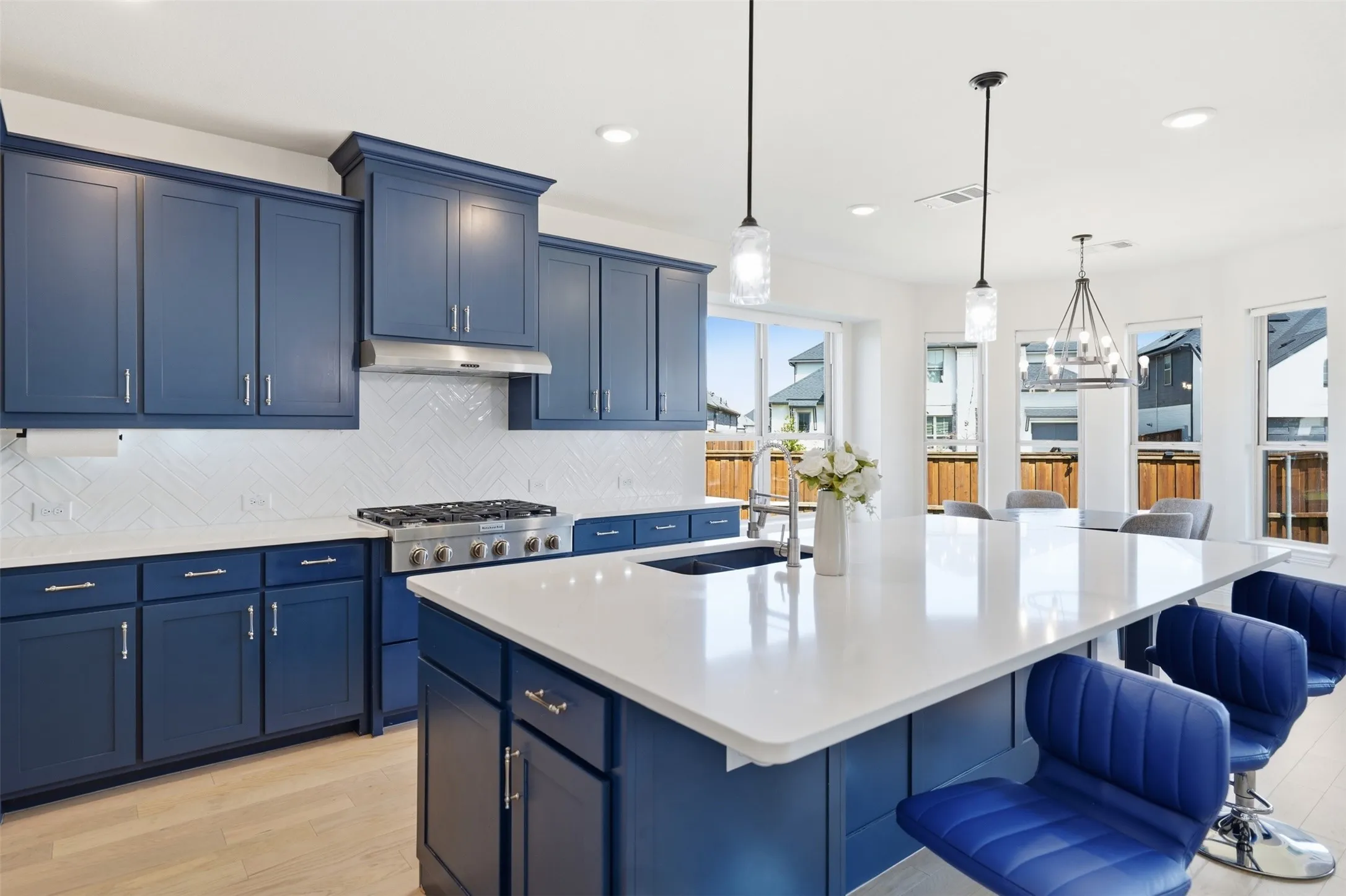 Gourmet kitchen featuring blue cabinetry, white countertops, a gas range with a stainless steel hood, an island with a sink, and pendant lighting