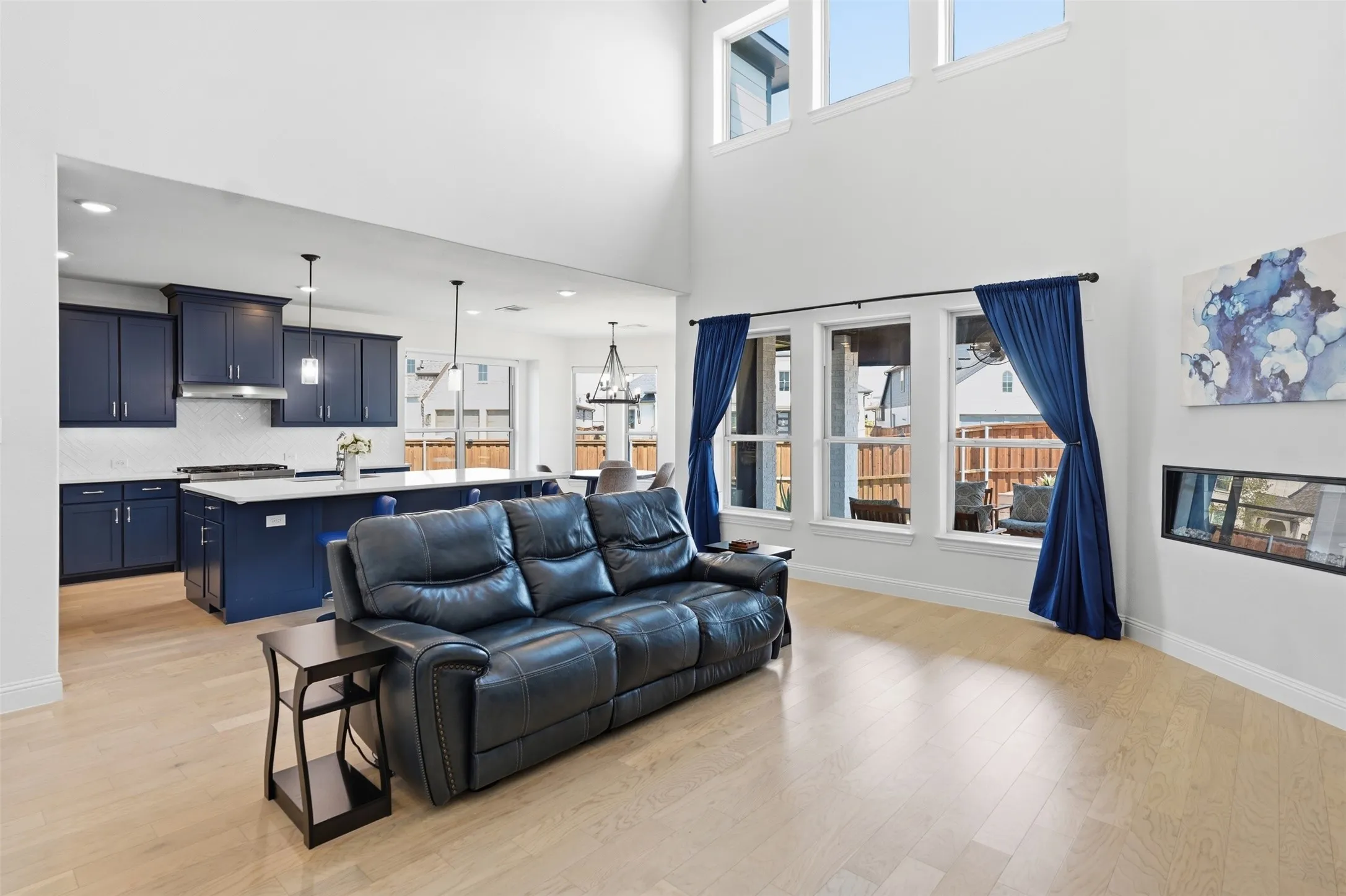 Expansive living area with high ceilings, light wood-finish flooring, and a linear fireplace