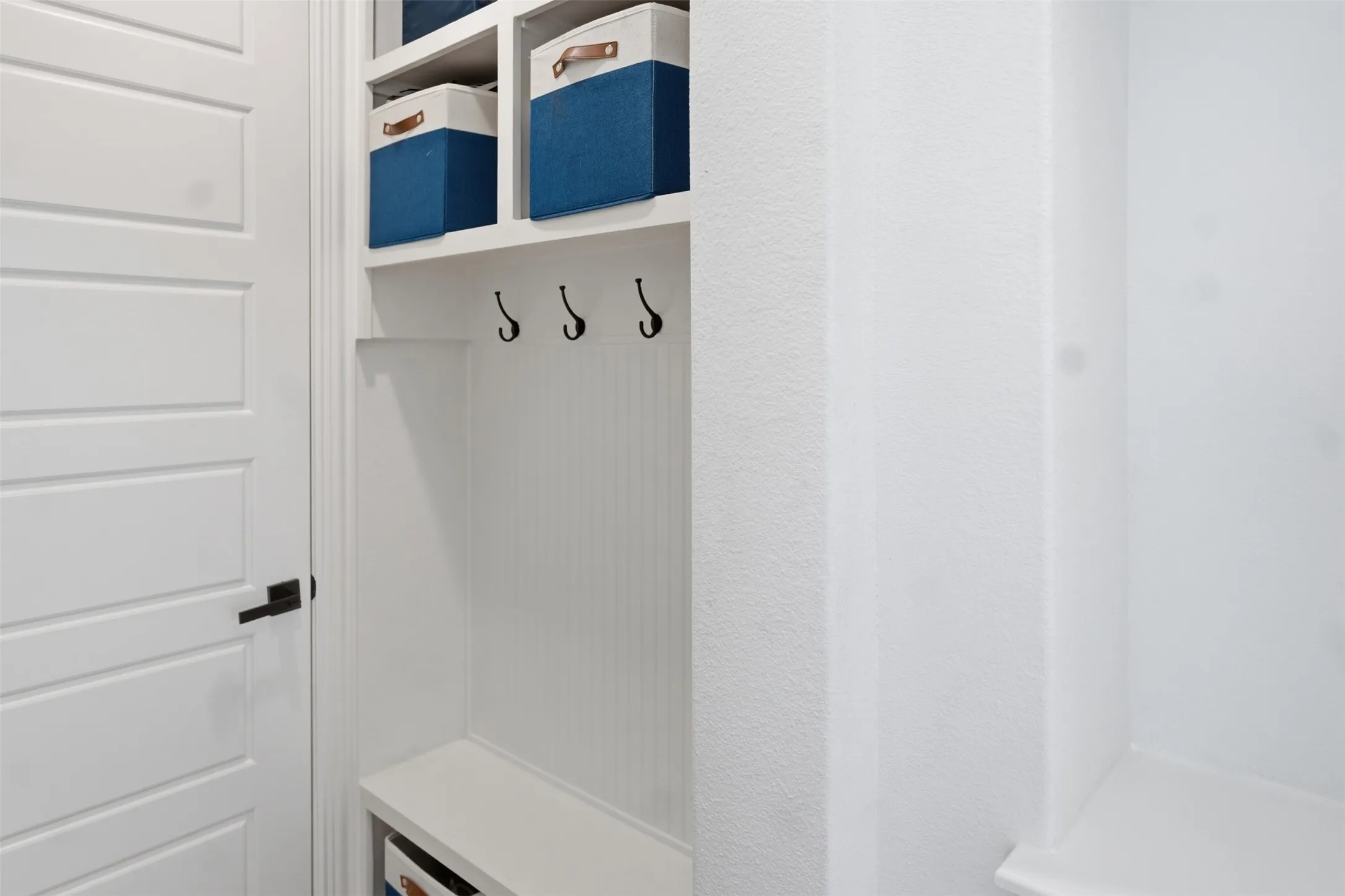 Built-in storage bench with beadboard paneling, upper shelving, and black coat hooks