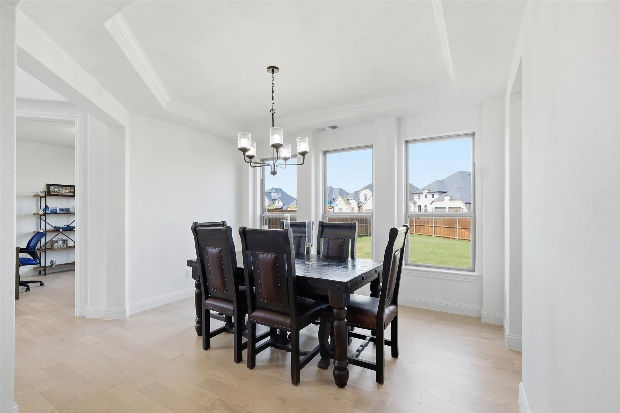 Tray ceiling with crown molding, chandelier with glass shades, wood-finish flooring, multiple windows, and a spacious backyard