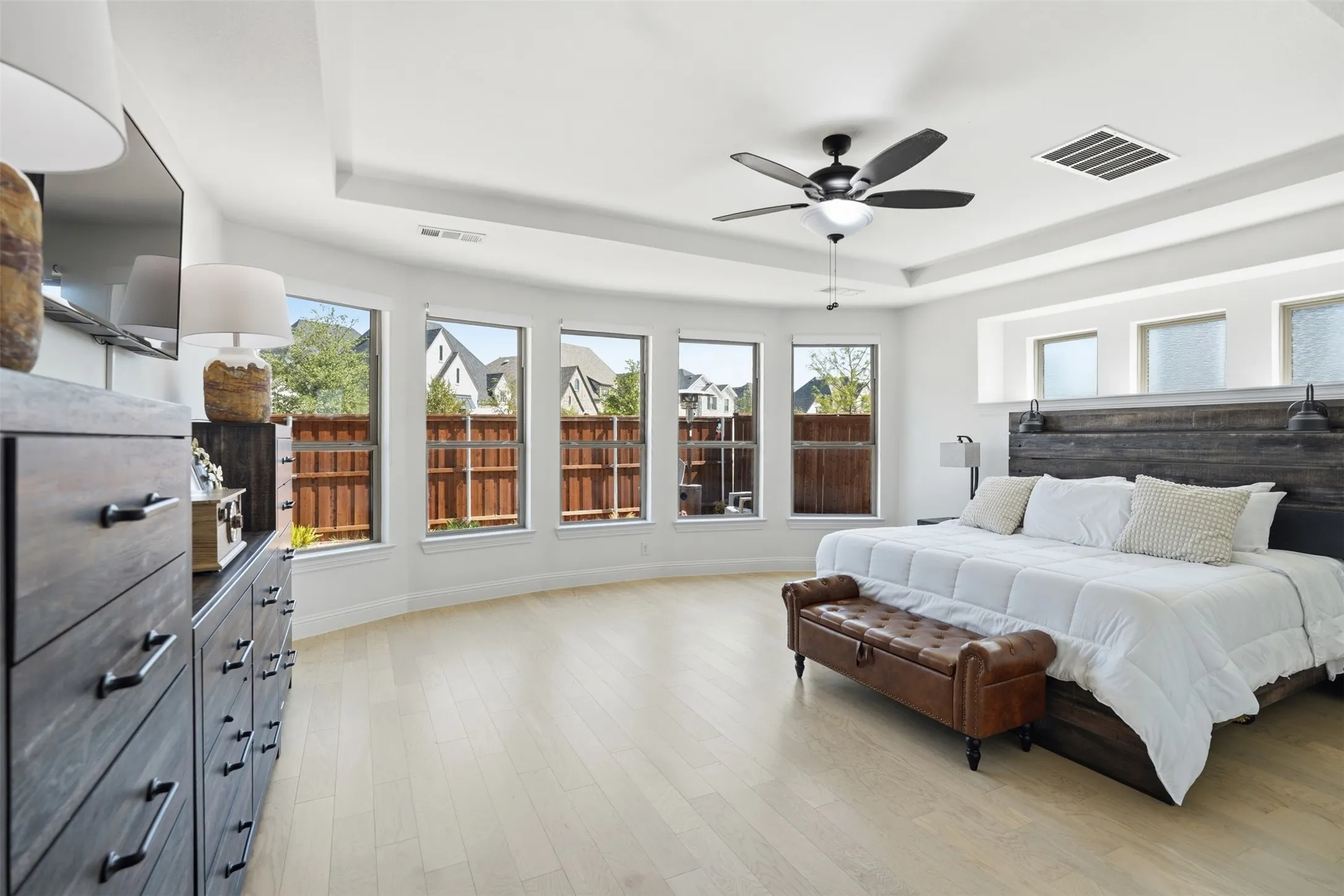 Tray ceiling with a ceiling fan, light wood-finish flooring, and multiple windows