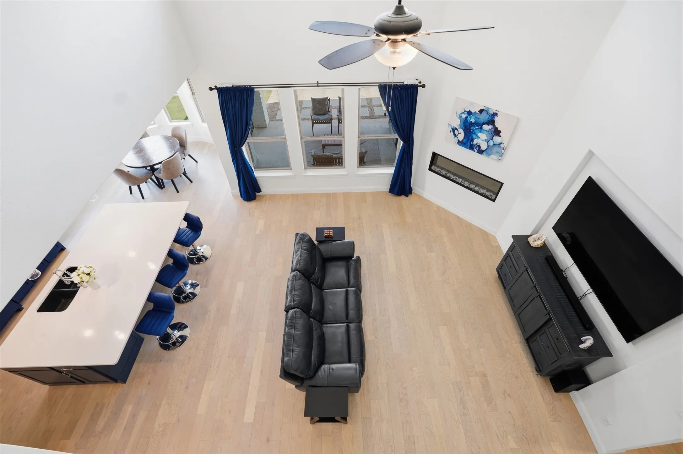 High ceilings with a ceiling fan, light wood-finish flooring, built-in linear fireplace, large kitchen island with countertop, and multiple windows