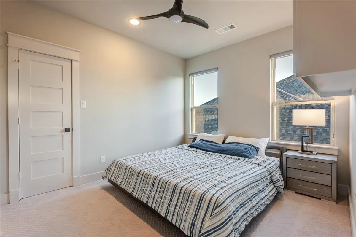 Ceiling fan, recessed lighting, two vertical windows, paneled interior door with dark hardware, and light-toned carpeting