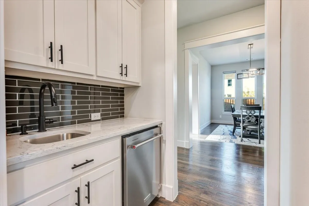 Custom beverage station with white cabinetry, a stainless steel sink, black subway tile backsplash, and a built-in stainless steel appliance
