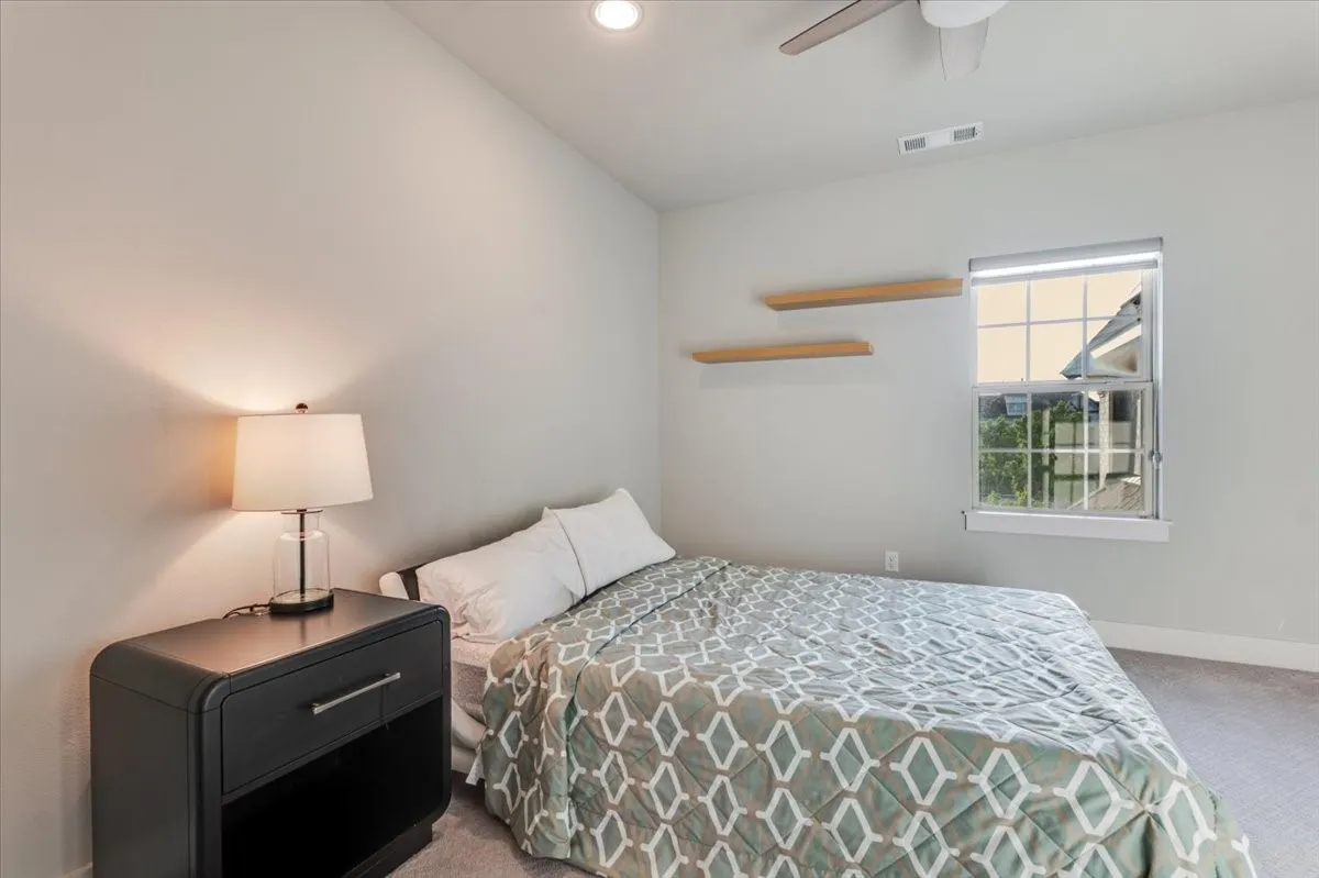 Recessed lighting, ceiling fan, window with roller shade, and two wall-mounted floating shelves