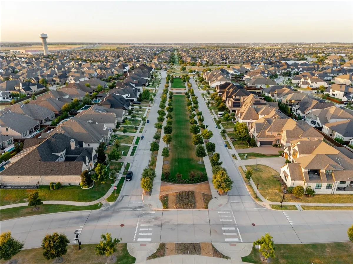 Residential neighborhood with mature trees, manicured lawns, and a central green space