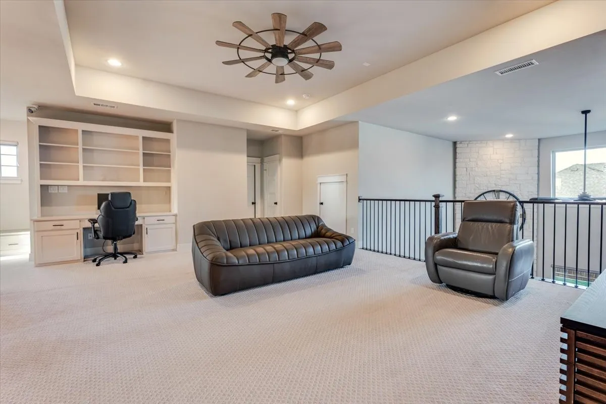 Expansive carpeted area featuring a built-in desk and shelving, ceiling fan, recessed lighting, and metal balusters