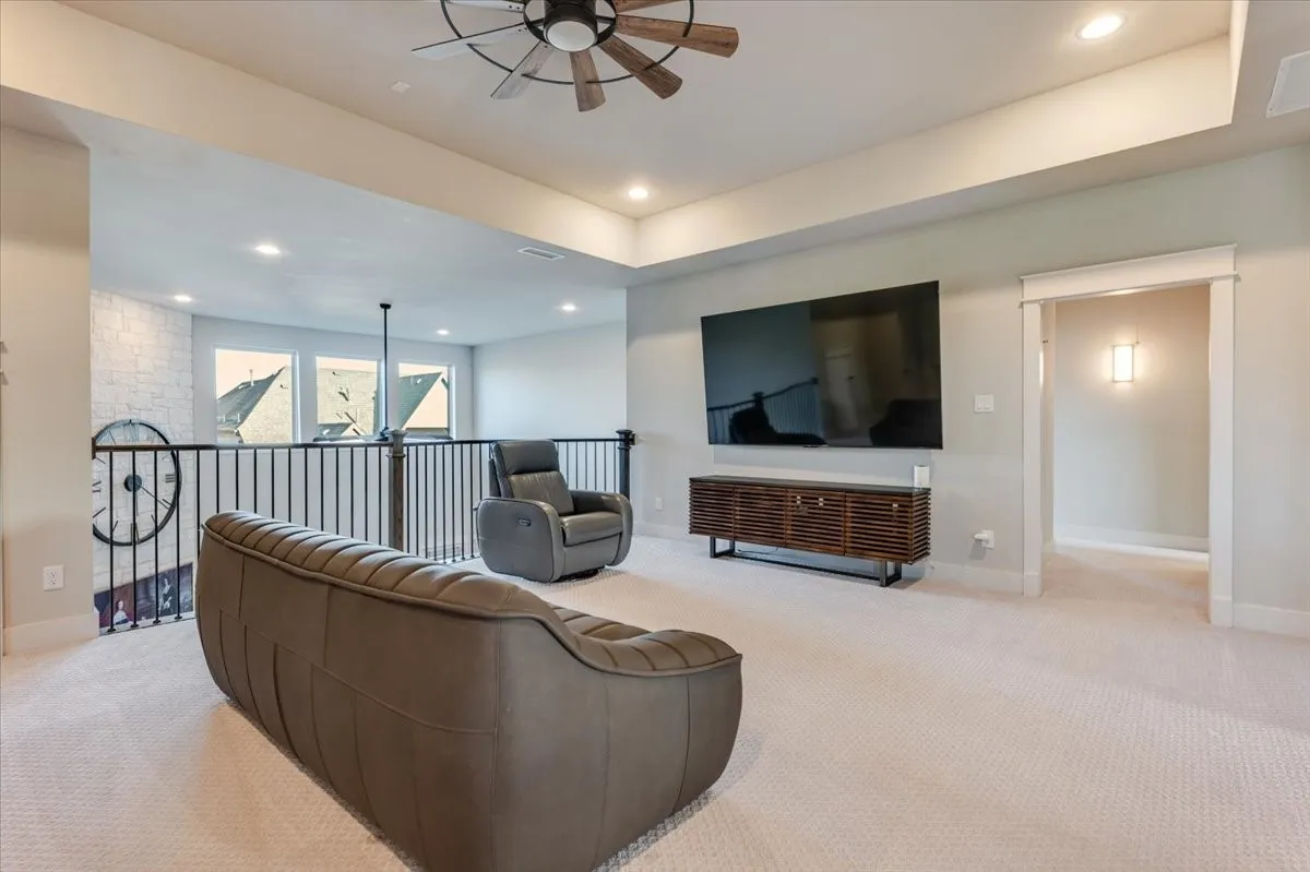 Carpeted loft area featuring a ceiling fan with wood-finish blades, recessed lighting, and a white brick-finish accent wall