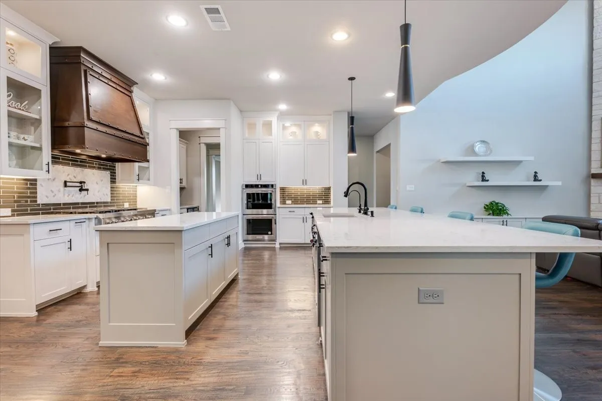Gourmet kitchen featuring white cabinetry, dual islands with light-toned countertops, integrated stainless steel appliances, and wood-finish flooring