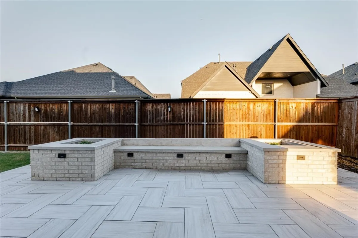 Expansive paver patio with a herringbone pattern, featuring a built-in brick seating area with integrated lighting and two planter boxes
