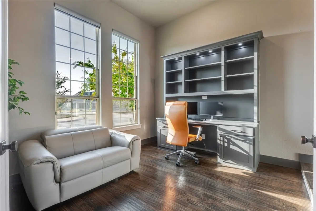 Built-in desk with integrated shelving and recessed lighting, accompanied by two tall windows, and wood-finish flooring