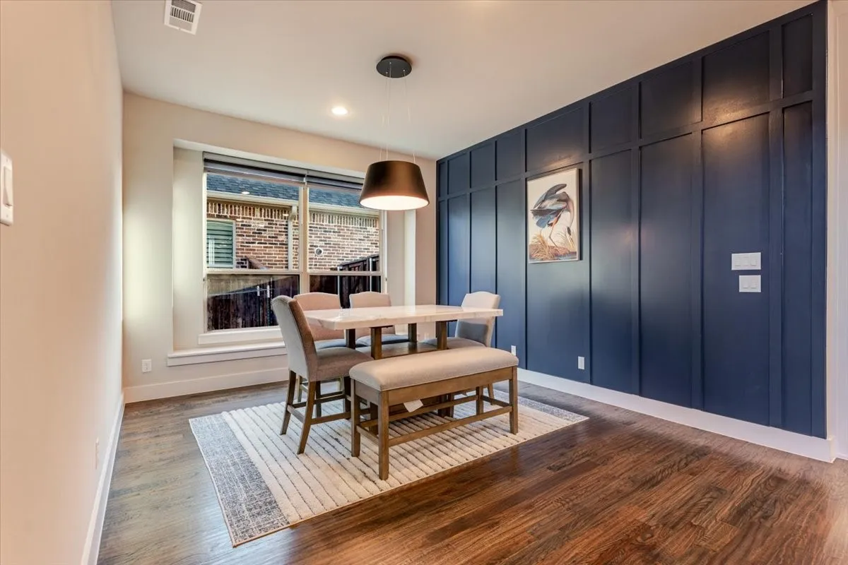 Dark wood-finish flooring, accent wall with decorative paneling, recessed lighting, and a modern pendant light fixture