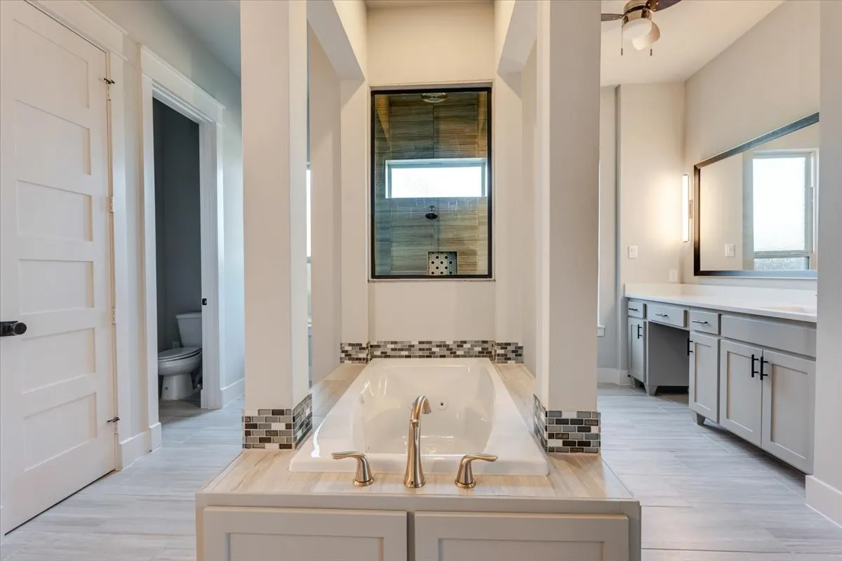 Soaking tub with mosaic tile accents, dual vanity with undermount sinks, and a walk-in shower with a transom window