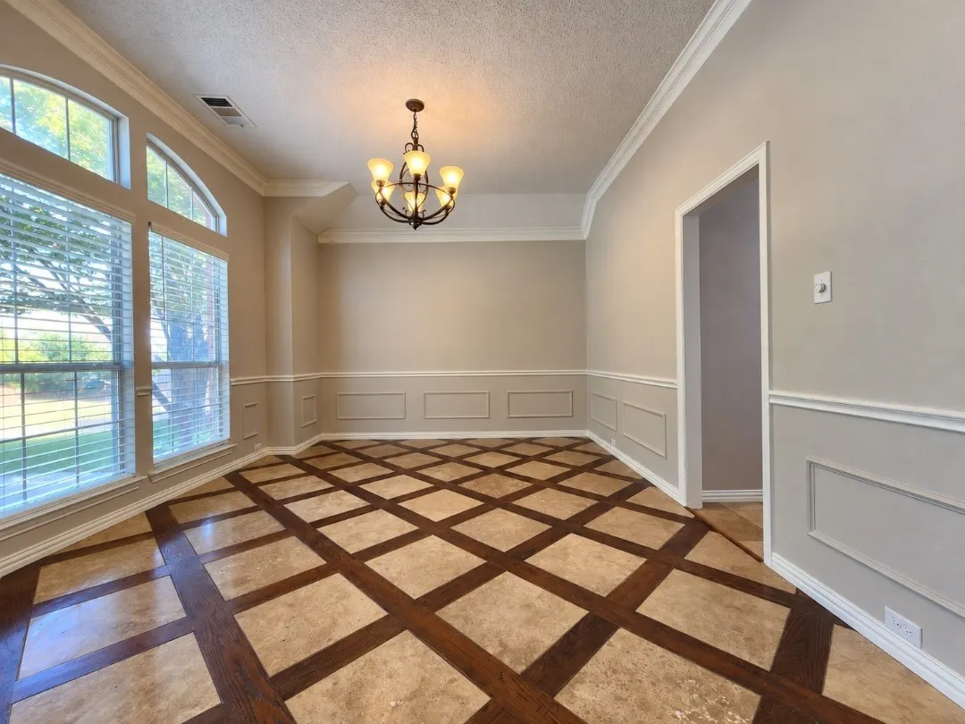 Patterned wood and stone-finish flooring, wainscoting with decorative trim, crown molding, arched transom window, and a five-light chandelier