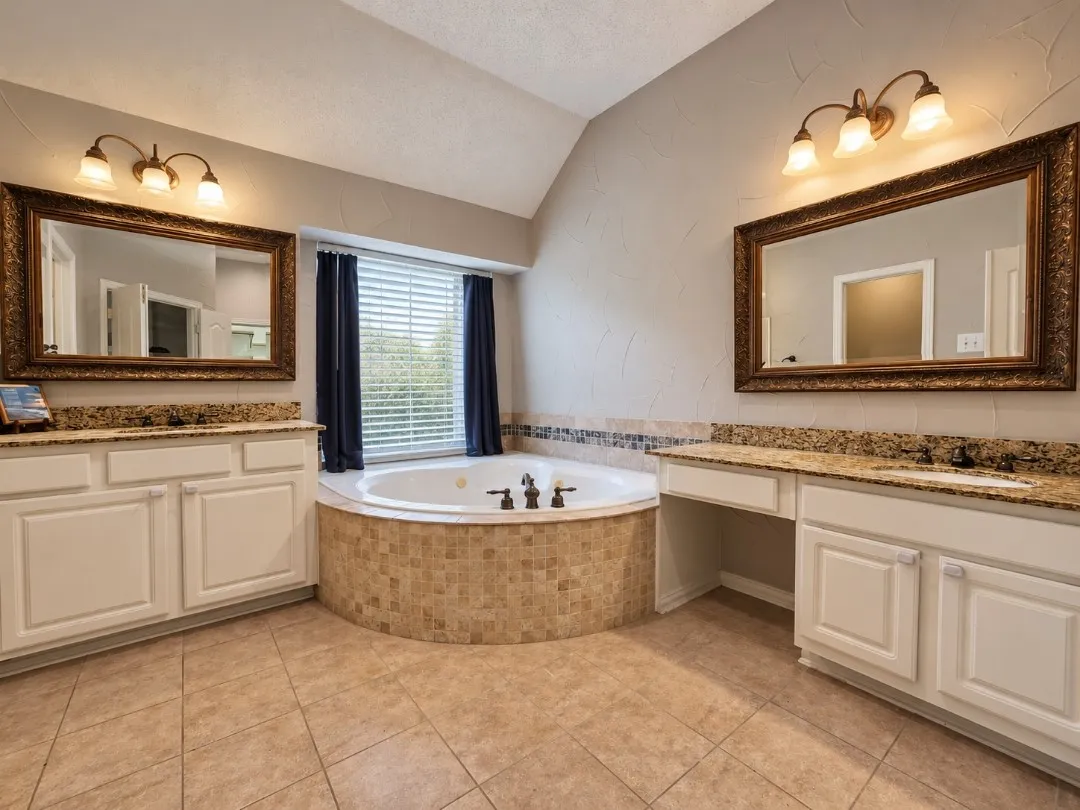 Dual vanity with granite countertops, integrated sinks, white cabinetry, and framed mirrors