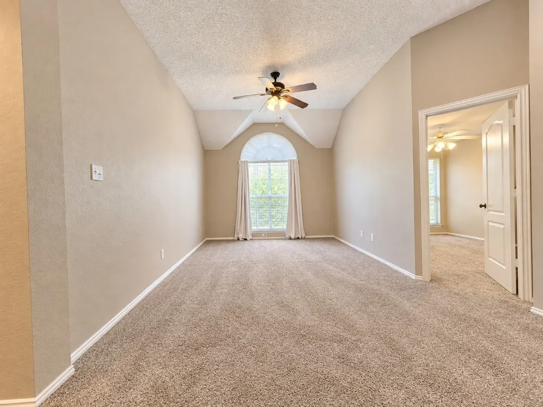 Vaulted ceiling with ceiling fan, arched window, and neutral-toned carpeting