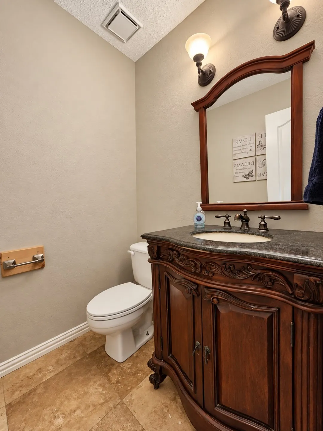 Ornate wood vanity with dark stone countertop, undermount sink, and bronze-finish fixtures