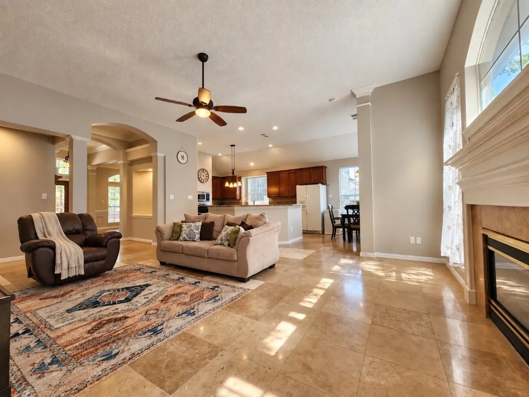 Spacious living area featuring tile flooring, a ceiling fan, and a fireplace with a mantel