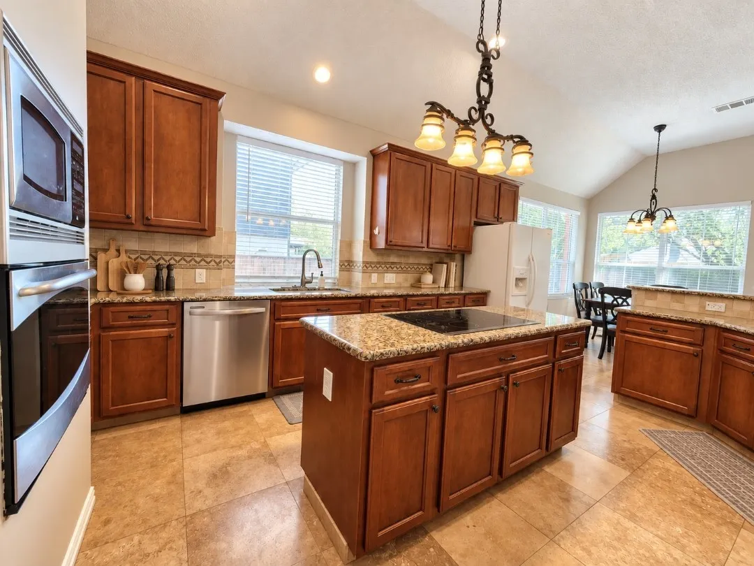 Kitchen featuring wood cabinetry, granite countertops, stainless steel appliances, a center island with a cooktop, and tile flooring