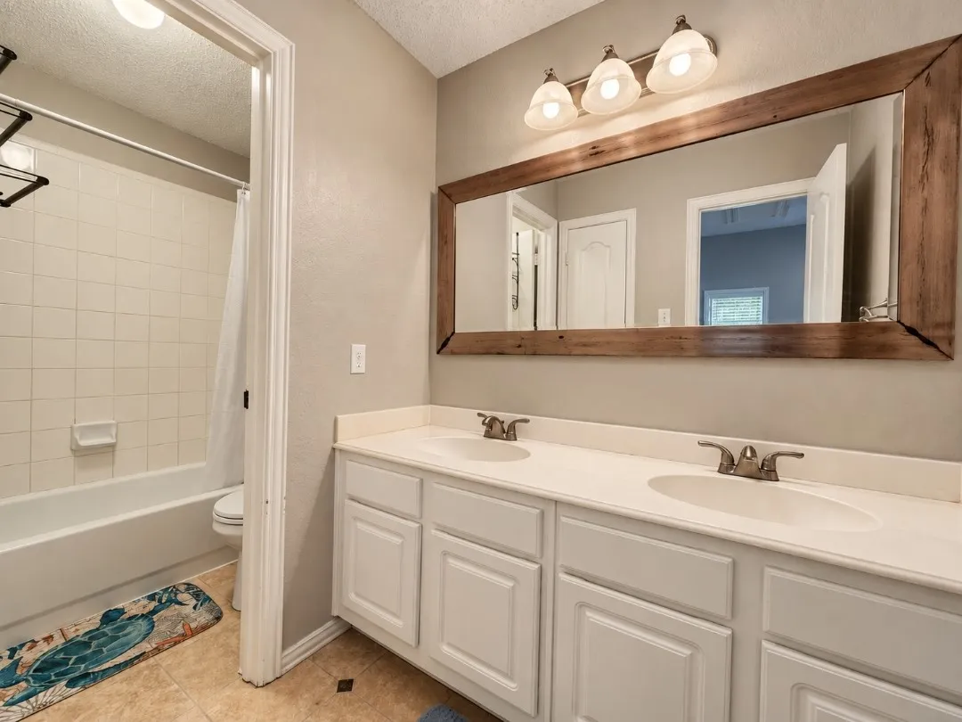 Dual vanity with white cabinetry, light-toned countertop, and a large wood-framed mirror