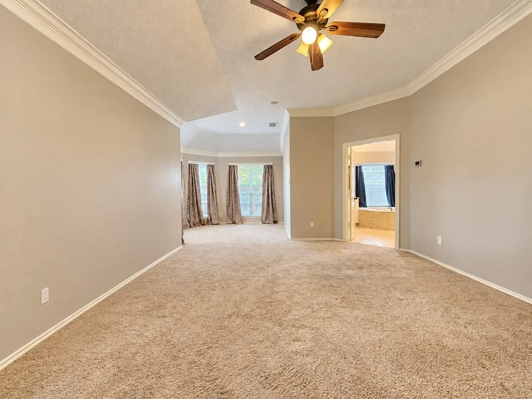 Tray ceiling with a ceiling fan, plush carpet flooring, crown molding, and bay windows