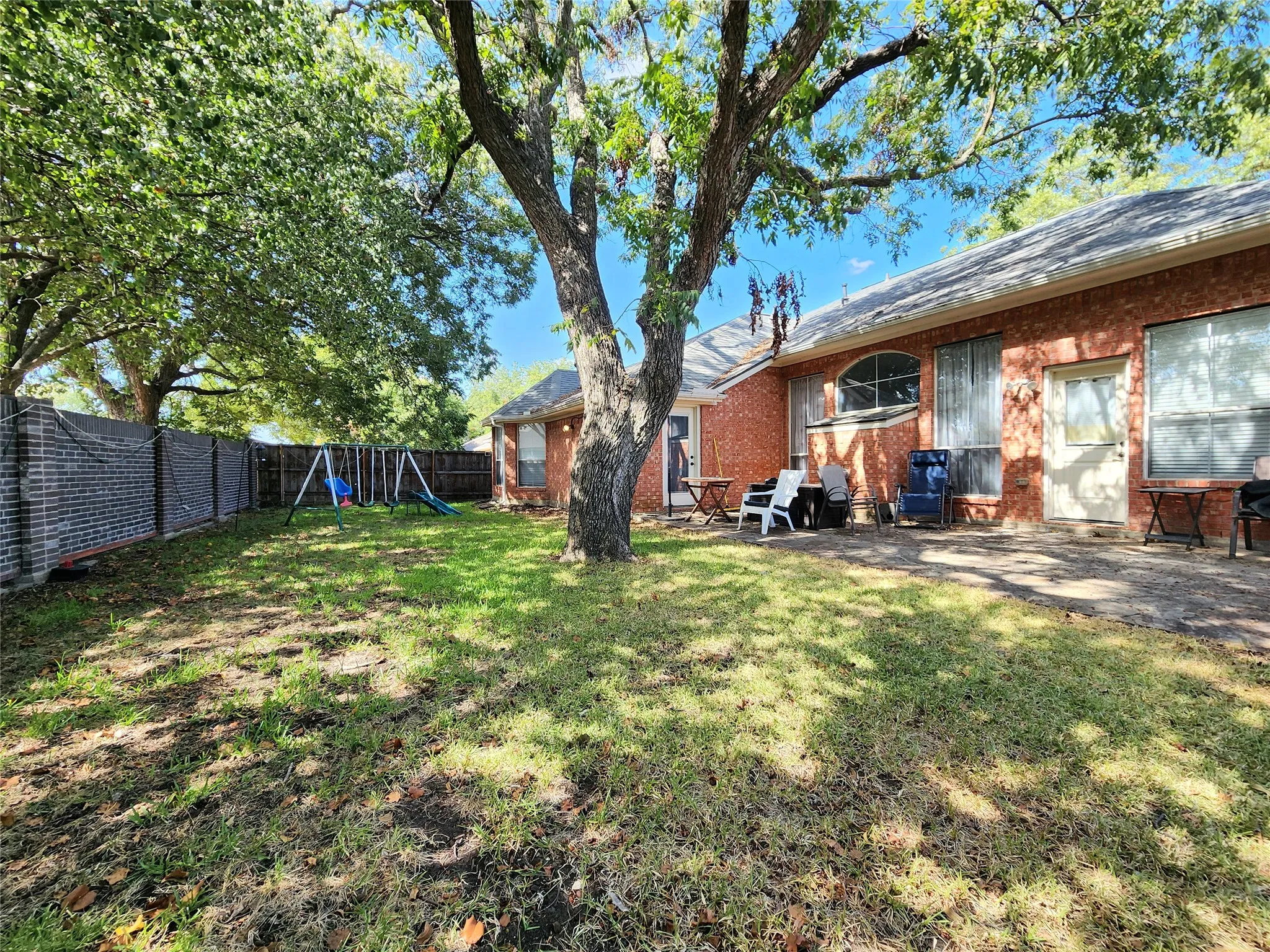 Expansive backyard featuring a mature tree, brick exterior, concrete patio, and a combination of brick and wood fencing