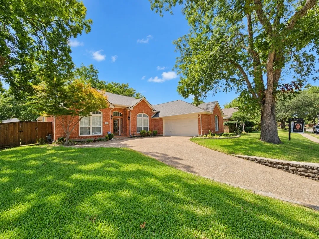 Brick exterior with arched window accents, attached two-car garage, mature trees, and a stone retaining wall